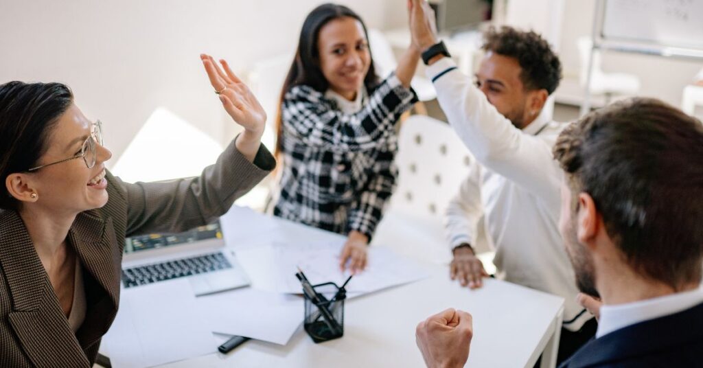 Photo of four employees smiling and high fiving each other