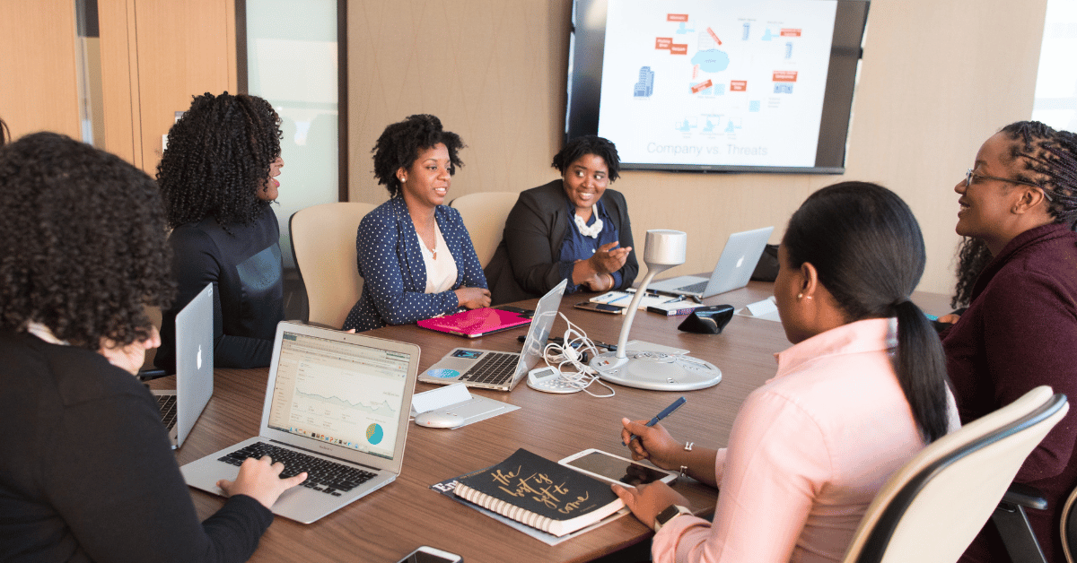 Photo of a corporate team meeting with women smiling at one another.