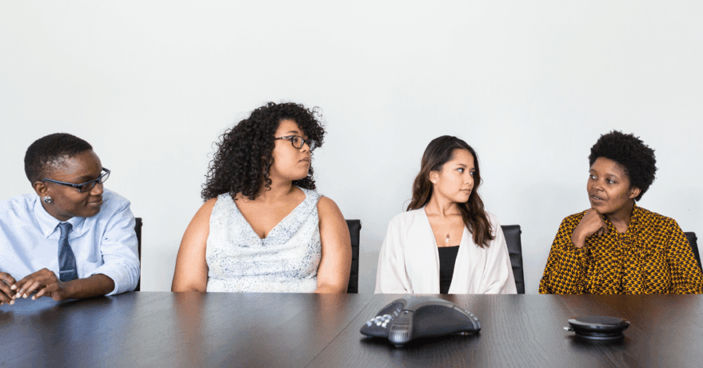 Photo of four employees at a conference table looking at each other and waiting for feedback.