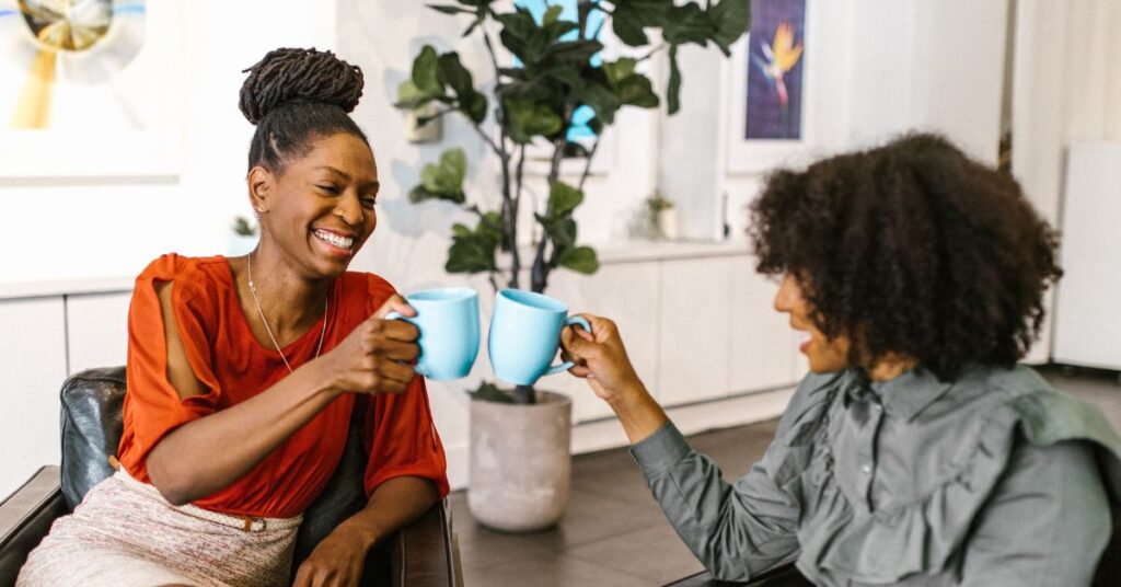 Photo of two women smiling and talking at work while clinking their coffee mugs together