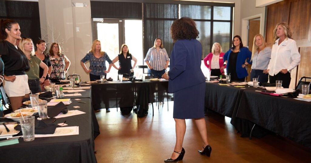 Michelle McKown-Campbell leading an energizing workshop session with women standing, engaging in an interactive confidence-building activity during a leadership event.