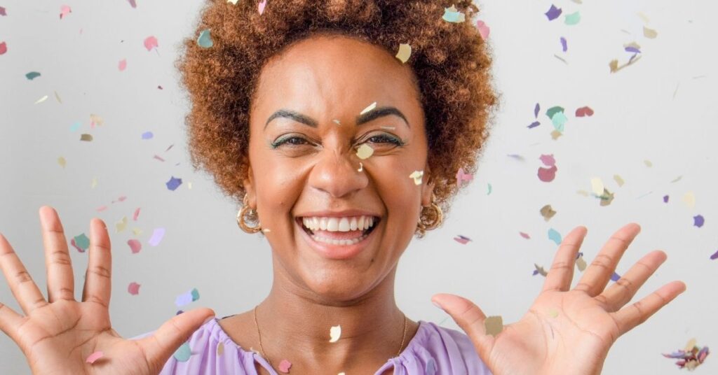 Smiling woman surrounded by confetti—capturing joy, self-celebration, and the empowering energy of recognizing personal wins at the start of a new year.