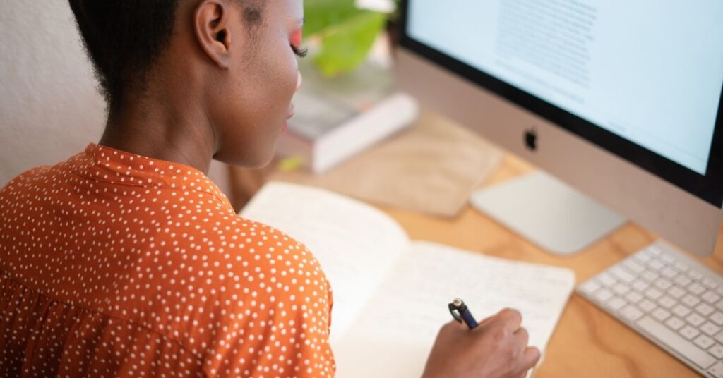 Woman journaling at her desk with a computer nearby—representing reflection, intention setting, and beginning the year with clarity and purpose.
