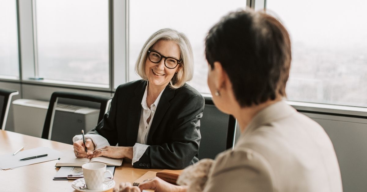 Two professional women having a warm, engaged conversation in a bright office setting—symbolizing connection, trust, and the power of relational leadership.